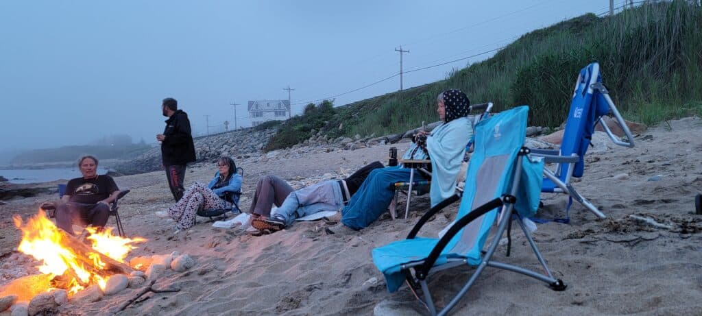 A family sits on a beach with a fire going on their East Coast family vacation to Block Island