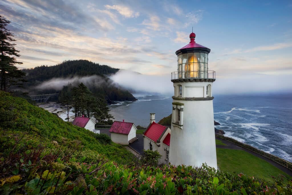 Family road trip ideas for Oregon, Hecate Head Lighthouse.  A stunning white lighthouse with red roof perched atop a craggy ocean cliff